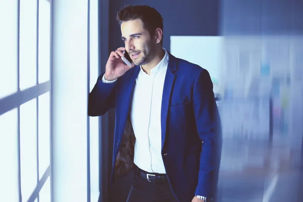 Hombre de negocios en traje hablando por teléfono y mirando hacia otro lado cerca de la ventana . — Foto de Stock