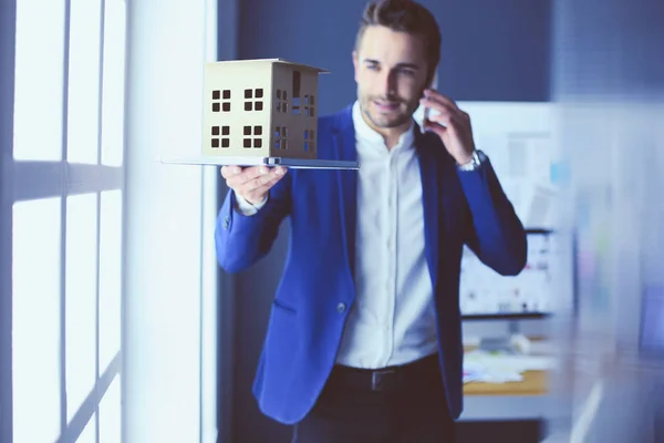 Businessman holding house miniature on hand standing in office.