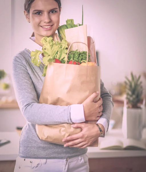 Giovane donna che tiene la spesa con verdure In piedi in cucina. — Foto Stock