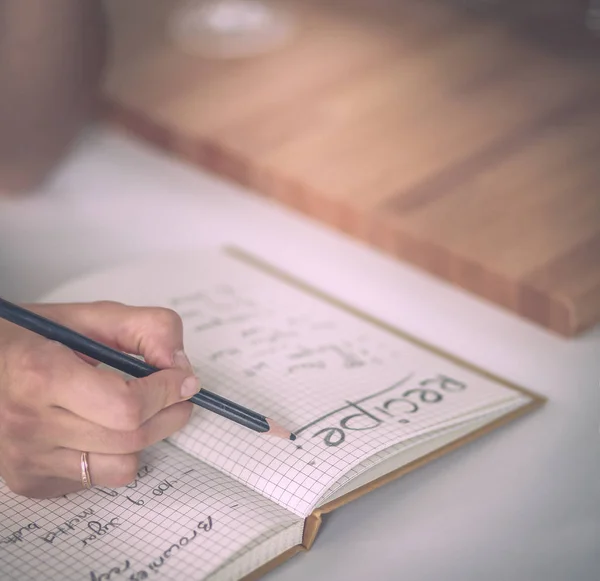 Happy beautiful woman standing in her kitchen writing on a notebook at home — Stock Photo, Image