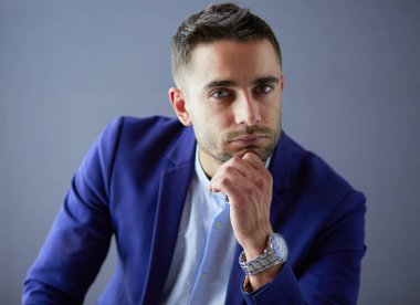 Gri arka planda yalnız oturan genç iş adamı.