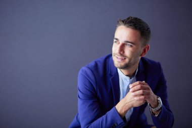 Gri arka planda yalnız oturan genç iş adamı.