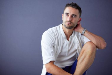 Gri arka planda yalnız oturan genç iş adamı.