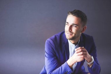 Gri arka planda yalnız oturan genç iş adamı.