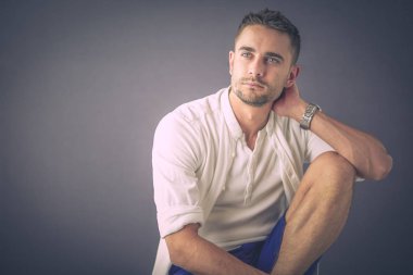 Gri arka planda yalnız oturan genç iş adamı.