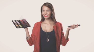 Genç ve güzel bir kadın bir elinde makyaj için boya ve gölgeli bir palet, makyaj için ikinci el fırça..