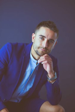 Gri arka planda yalnız oturan genç iş adamı.