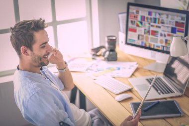 İnternette çalışırken bilgisayarın ve dizüstü bilgisayarın önünde grafik stüdyosunda oturan genç tasarımcının portresi.