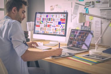 İnternette çalışırken bilgisayarın ve dizüstü bilgisayarın önünde grafik stüdyosunda oturan genç tasarımcının portresi.