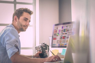 İnternette çalışırken bilgisayarın ve dizüstü bilgisayarın önünde grafik stüdyosunda oturan genç tasarımcının portresi.