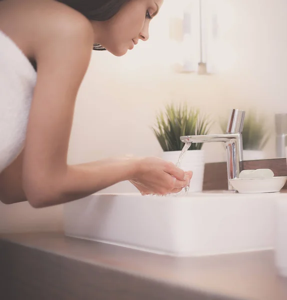 Mujer joven lavándose la cara con agua limpia en el baño —  Fotos de Stock