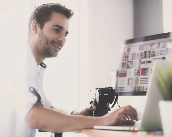 Retrato del joven diseñador sentado en el estudio gráfico frente a la computadora portátil y el ordenador mientras trabaja en línea. — Foto de Stock