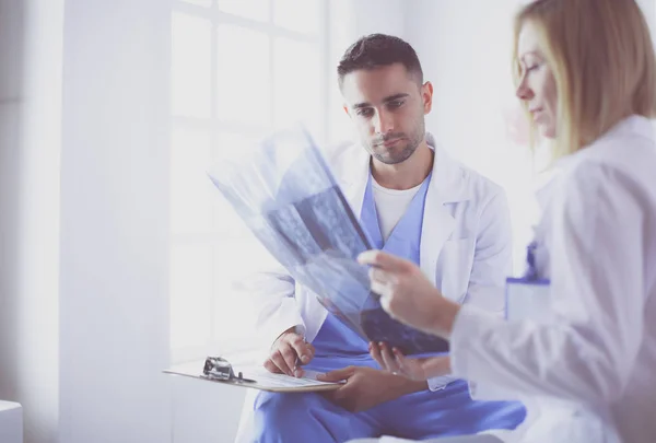 Médico bonito está conversando com jovem médica e fazendo anotações enquanto está sentado em seu escritório. — Fotografia de Stock