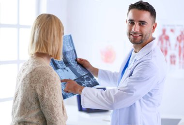 Yakışıklı doktor genç bayan hastasıyla konuşuyor ve ofisinde otururken notlar alıyor..