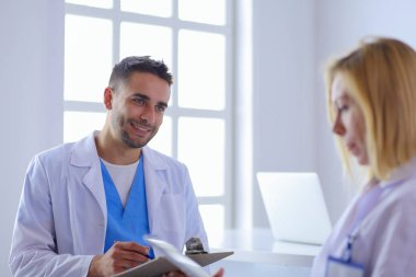 Yakışıklı doktor genç bayan doktorla konuşuyor ve ofisinde otururken notlar alıyor..