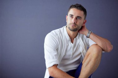 Gri arka planda yalnız oturan genç iş adamı.