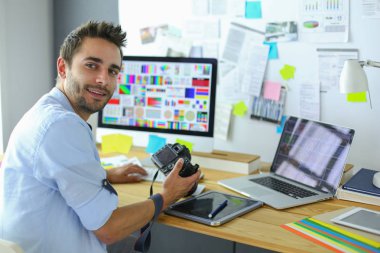 İnternette çalışırken bilgisayarın ve dizüstü bilgisayarın önünde grafik stüdyosunda oturan genç tasarımcının portresi.