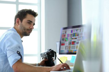 İnternette çalışırken bilgisayarın ve dizüstü bilgisayarın önünde grafik stüdyosunda oturan genç tasarımcının portresi.