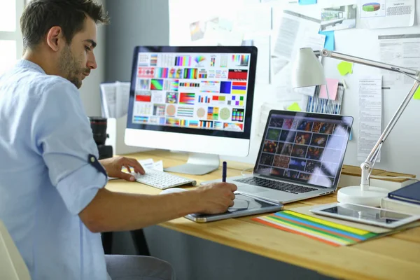 Porträt eines jungen Designers, der im Grafikstudio vor Laptop und Computer sitzt, während er online arbeitet. — Stockfoto