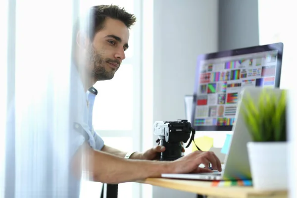 Retrato del joven diseñador sentado en el estudio gráfico frente a la computadora portátil y el ordenador mientras trabaja en línea. — Foto de Stock