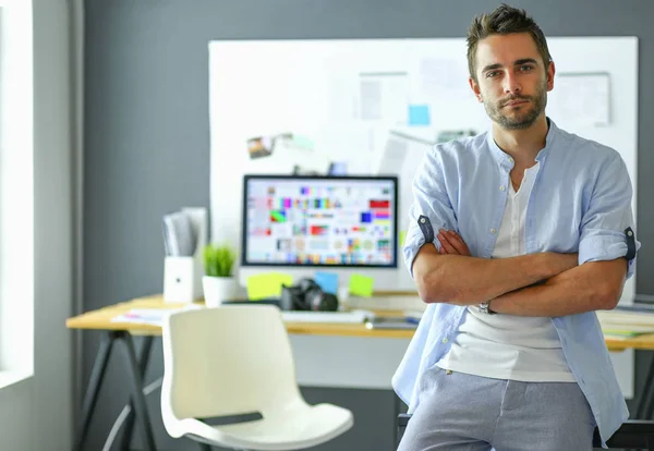 Porträt eines jungen Designers vor Laptop und Computer während der Arbeit. Assistentin bedient ihr Handy im Hintergrund. — Stockfoto