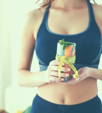 Elinde bardak dolusu taze meyve salatası ve bardağın etrafında mezura tutan bir kadın.