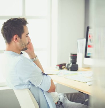İnternette çalışırken bilgisayarın ve dizüstü bilgisayarın önünde grafik stüdyosunda oturan genç tasarımcının portresi.