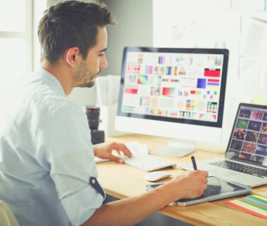 İnternette çalışırken bilgisayarın ve dizüstü bilgisayarın önünde grafik stüdyosunda oturan genç tasarımcının portresi.