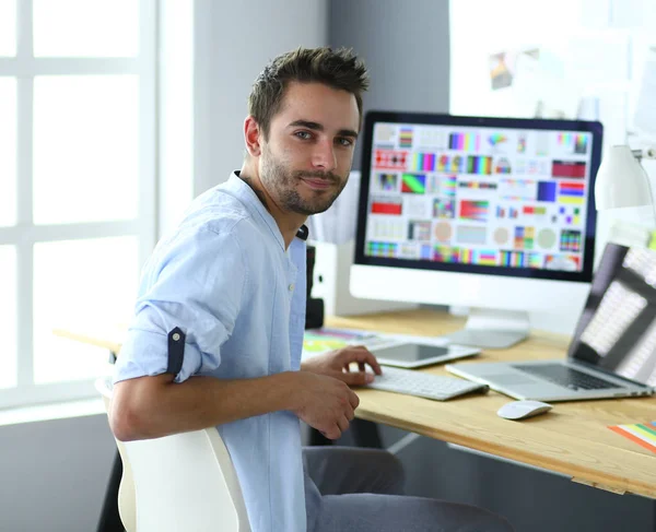 Porträt eines jungen Designers, der im Grafikstudio vor Laptop und Computer sitzt, während er online arbeitet. — Stockfoto