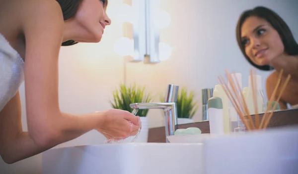 Mujer joven lavándose la cara con agua limpia en el baño — Foto de Stock