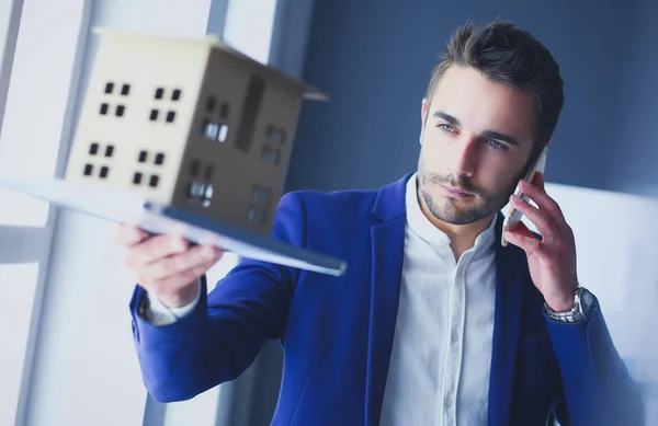 Homme d'affaires tenant maison miniature à portée de main debout dans le bureau . — Photo