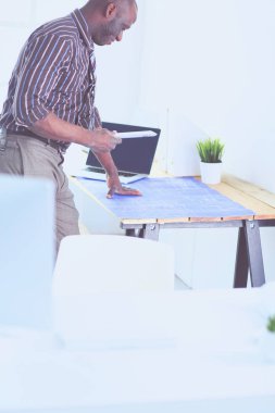 Ofiste bilgisayar ve planlarla çalışan Afrikalı Amerikalı bir mimar.