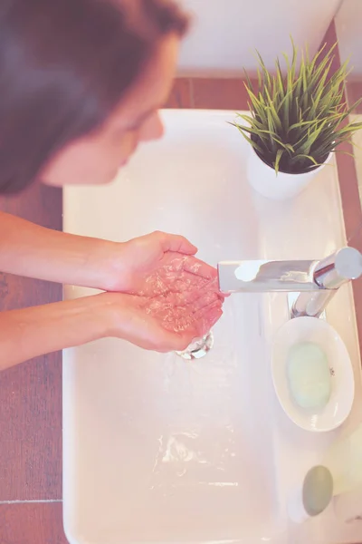 Giovane donna che si lava il viso con acqua pulita in bagno — Foto Stock