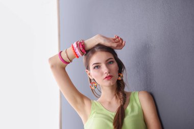 Gri duvarda gülümseyen genç bir kadının portresi.