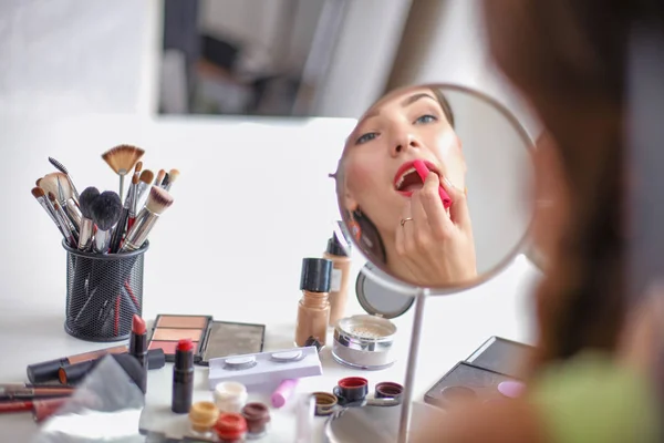 Joven hermosa mujer haciendo maquillaje cerca del espejo, sentado en el escritorio —  Fotos de Stock