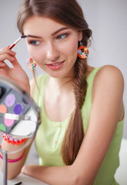 Joven hermosa mujer haciendo maquillaje cerca del espejo, sentado en el escritorio — Foto de Stock