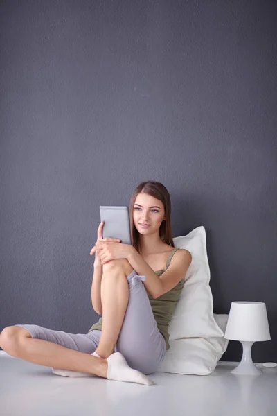 Mujer morena bonita sentada en el suelo con una almohada y mesa de avión — Foto de Stock