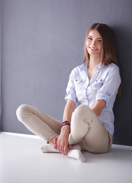 Portrait of a casual happy woman sitting on the floor on gray background — Stock Photo, Image
