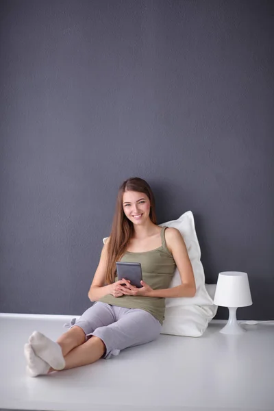 Hezká brunetka ženu sedící na podlaze s polštářem a letadlo tabulka — Stock fotografie