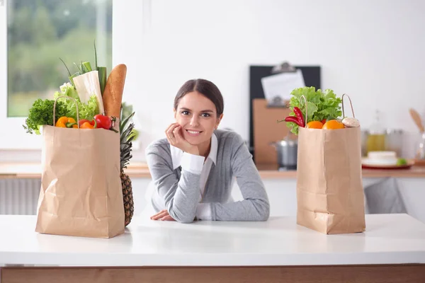 Giovane donna che tiene la borsa della spesa con verdure. In piedi in cucina — Foto Stock