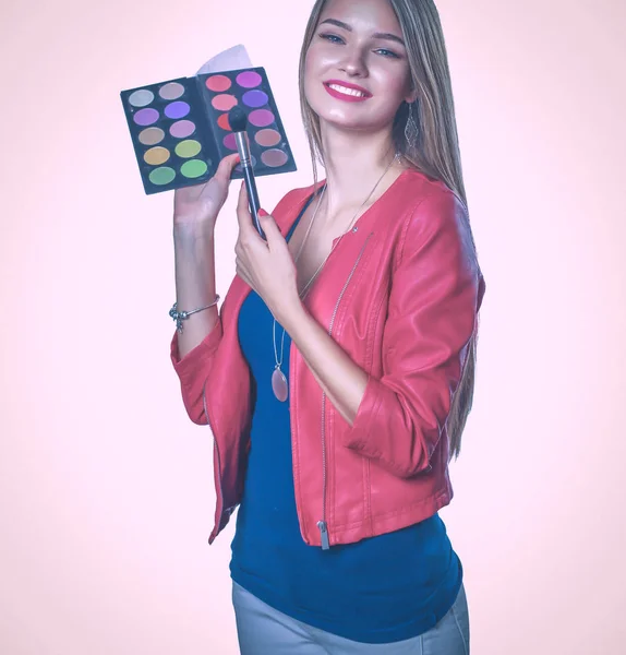 Jeune belle femme tient dans une main et une palette avec de la peinture et des ombres pour le maquillage, brosse d'occasion pour le maquillage — Photo