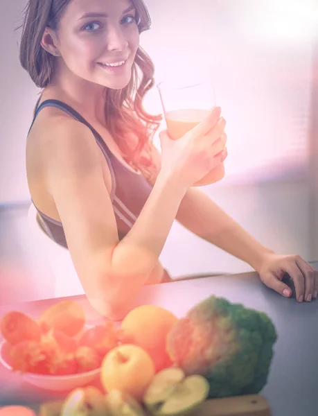 Fille assise dans la cuisine sur le bureau avec des fruits et des verres avec du jus — Photo