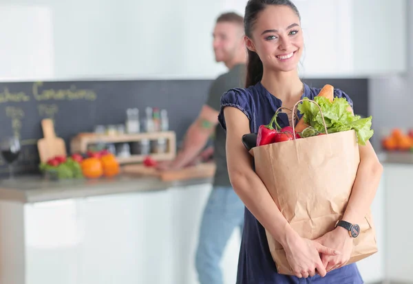 Pareja joven en la cocina, mujer con una bolsa de compras — Foto de Stock