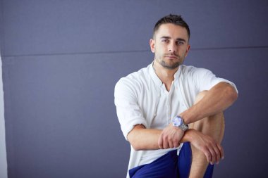 Gri arka planda yalnız oturan genç iş adamı.