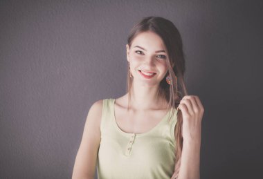 Gri duvarda gülümseyen genç bir kadının portresi.