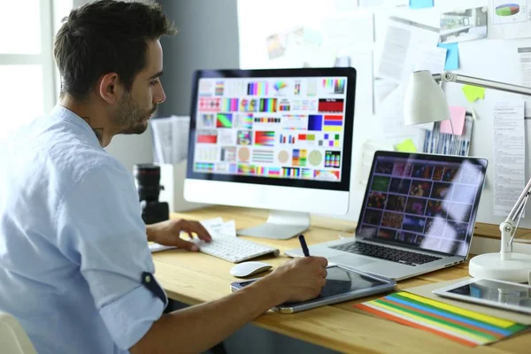 Retrato de jovem designer sentado no estúdio gráfico na frente de laptop e computador enquanto trabalhava online. — Fotografia de Stock