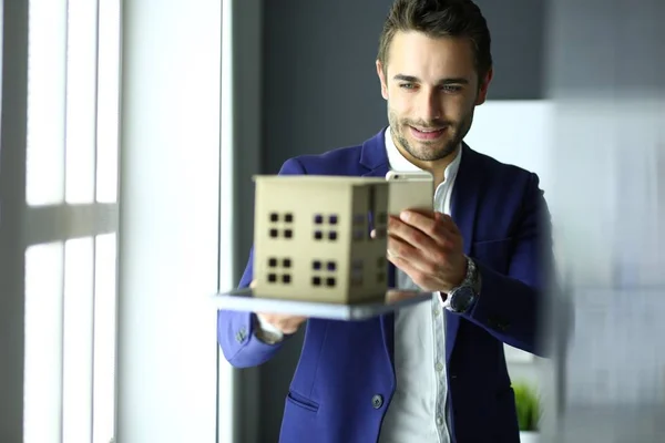 Homme d'affaires tenant maison miniature à portée de main debout dans le bureau . — Photo