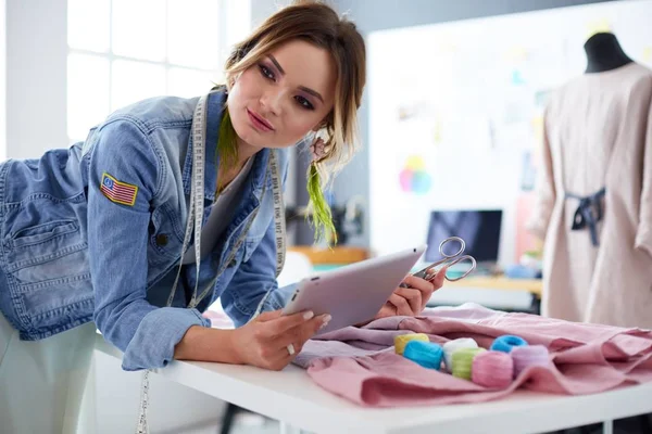 Mulher designer de moda trabalhando com ipad em seus projetos no estúdio — Fotografia de Stock