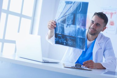 Yakışıklı doktor genç bayan hastasıyla konuşuyor ve ofisinde otururken notlar alıyor..