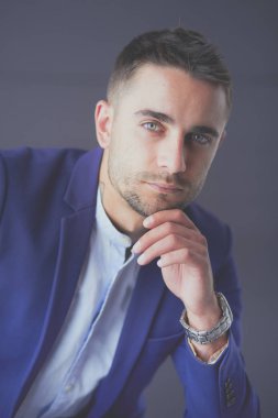 Gri arka planda yalnız oturan genç iş adamı.